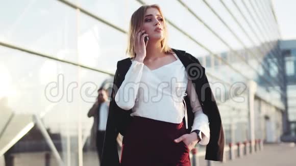 自信的金发女郎站在机场候机楼旁用电话交谈检查时间抚摸她视频的预览图