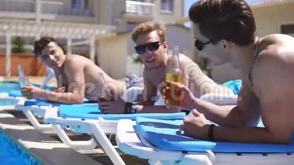 一群年轻朋友喝着啤酒躺在游泳池旁边的教练身上放松慢镜头视频的预览图