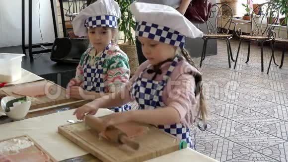 两个穿制服的小女孩厨师学着用擀面杖在木板上擀面视频的预览图