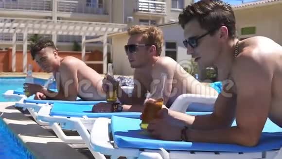 一群年轻朋友喝着啤酒躺在游泳池旁边的教练身上放松慢镜头视频的预览图