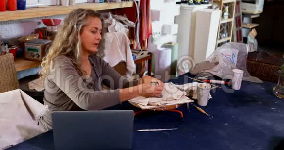 成熟的女性陶工在使用笔记本电脑4k的同时塑造粘土视频的预览图
