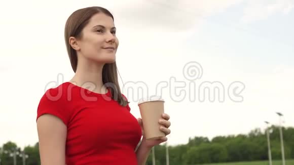 女人在公园里散步喝咖啡放松暑假微笑面对背景天空视频的预览图