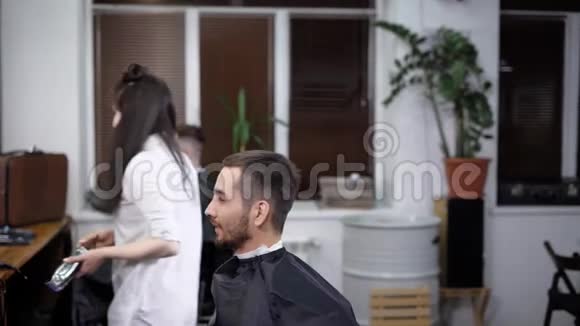 女性和男性理发师正在理发店与切割斗篷的客户合作年轻女子用剪发机视频的预览图