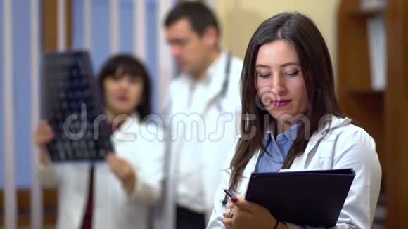 女医生手里拿着一个文件夹在背景中医生检查了x射线视频的预览图