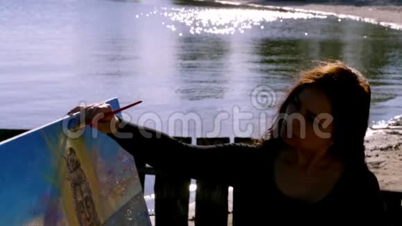 夏天河边海滩上日出时一位美丽的女艺术家手里拿着画笔画了一幅画她是个女人视频的预览图