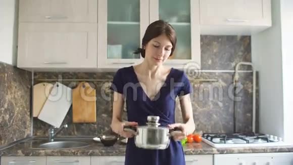 一个年轻女孩在家厨房做饭时摇晃着打开一个沙锅的画像视频的预览图