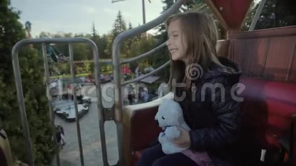 有趣的女孩骑在环形交叉路口上微笑着在秋天快乐地拥抱她的泰迪熊穿着宽松的衣服视频的预览图
