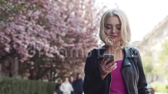 美丽的年轻女子走在樱花盛开的小巷里上网幸福地微笑着走向视频的预览图