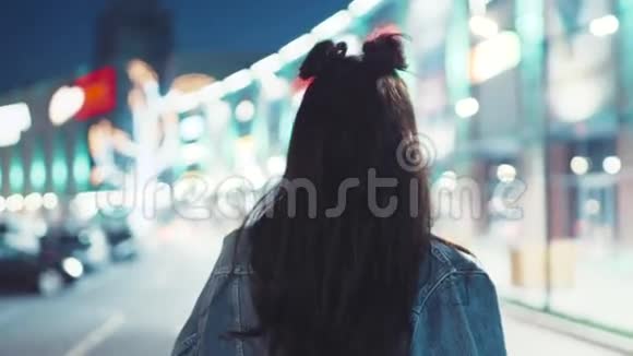 年轻的黑发女孩穿着牛仔裤夹克和时髦的发型红唇在夜城里徘徊转向视频的预览图