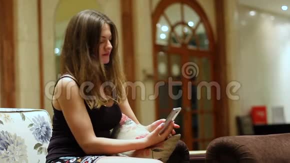 一位漂亮的黑发女郎在一家昂贵的酒店大厅的新智能手机上自拍美丽的女孩在拍照片视频的预览图
