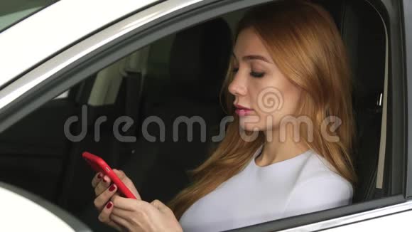 漂亮的年轻女人坐在车里用智能手机视频的预览图
