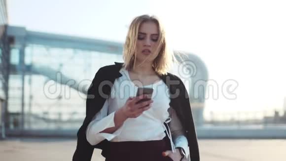 漂亮的金发女人走在商业中心附近在电话里交谈时尚的外观优雅的白色衬衫视频的预览图