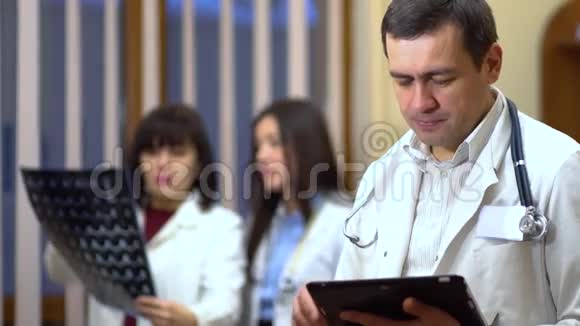 一位男医生自信地看着相机在背景中医生正在检查X光视频的预览图