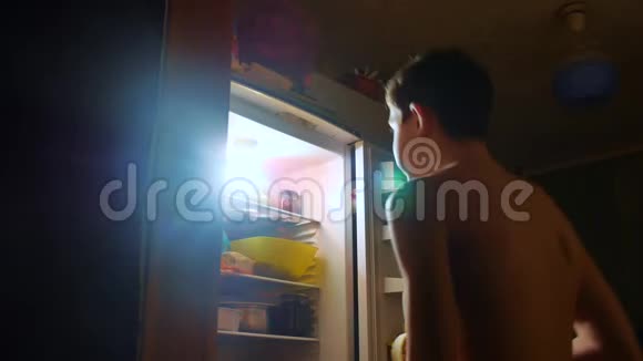 小男孩晚上从冰箱里吃饥饿和饕餮青少年男孩晚上看冰箱饕餮视频的预览图