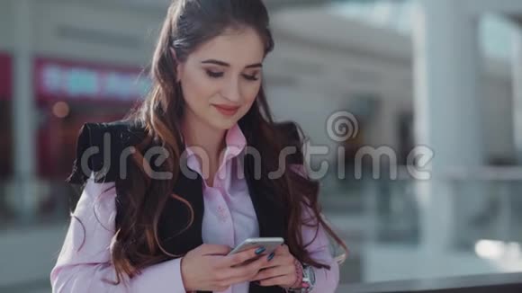漂亮的年轻女人穿着粉红色衬衫化妆漂亮在购物中心她微笑着发短信视频的预览图