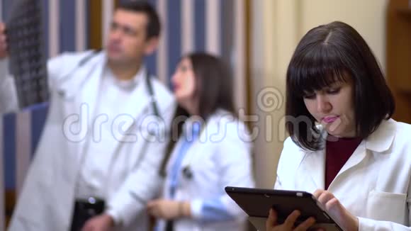 一位女医生自信地看着相机在背景中医生正在检查X光视频的预览图