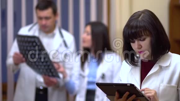 一位女医生自信地看着相机在背景中医生正在检查X光视频的预览图