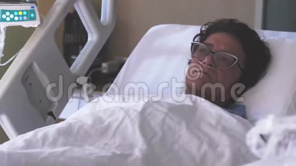 一位年老戴眼镜的患病女性患者在带有静脉滴注室的病房里受苦3840x2160视频的预览图