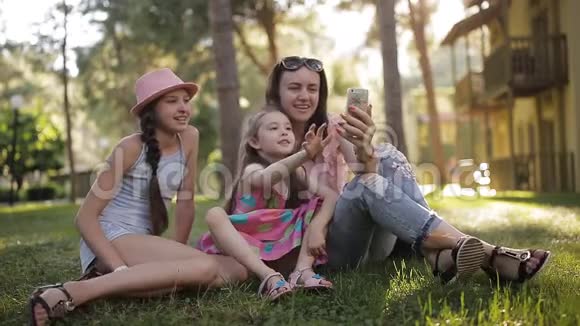 妈妈和两个女儿坐在草地上用电话通过视频交流视频的预览图