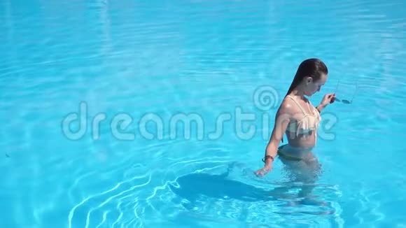 穿着漂亮泳衣的年轻女子在游泳池里戴上太阳镜视频的预览图