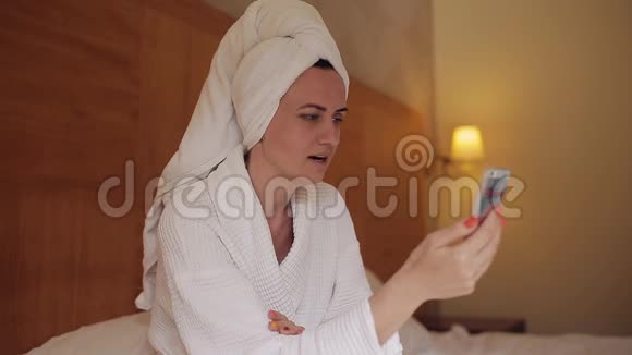 一个穿着浴袍的女孩坐在床上用手机与朋友交流视频的预览图
