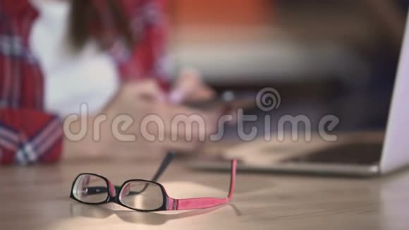 时尚眼镜放在桌子上女人在智能手机上发短信交流视频的预览图