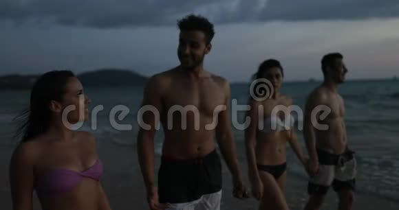 在夕阳下的沙滩上散步的快乐朋友小组海边度假时的年轻人交流视频的预览图