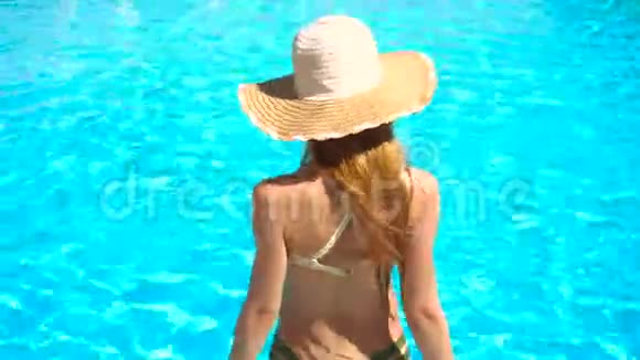 穿着泳衣和帽子的年轻女孩走进游泳池的水中视频的预览图