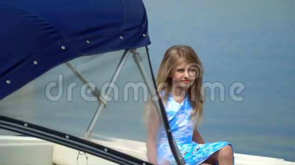 可爱的小女孩在码头的水面上摆姿势拍照有一点金发女孩坐在船上视频的预览图