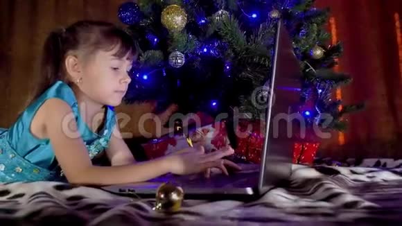 圣诞树下有笔记本电脑的女孩在新年里孩子在一棵树下手提电脑树下的一个小女孩视频的预览图