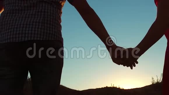 一对情侣的剪影手牵手走向太阳在夕阳下戏剧性的天空背景年轻幸福的一对走视频的预览图