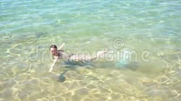 美丽的年轻女孩穿着泳衣漂浮在海里看着相机微笑着视频的预览图