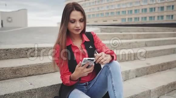 女人坐在户外的台阶上用智能手机说话视频的预览图
