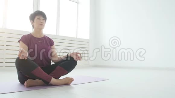 和谐体育和健康的概念中年妇女在白色的室内做瑜伽视频的预览图