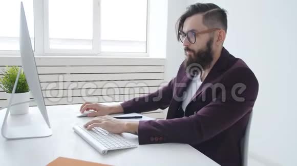 办公室工作或自由职业者的概念年轻的留胡子的时髦男人在办公室的电脑里工作视频的预览图