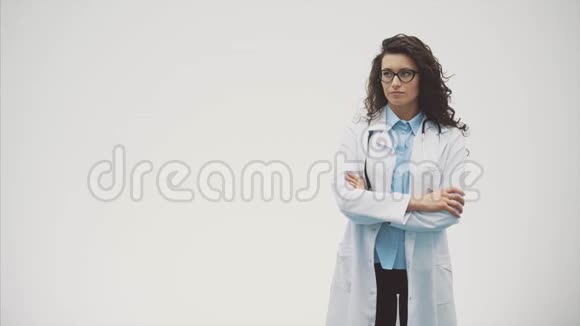美丽的年轻黑发医生穿着医疗制服在孤立的灰色背景在这段时间里听音器视频的预览图