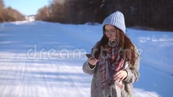 女孩在冬天的森林附近的道路上在她的手机上阅读新闻视频的预览图