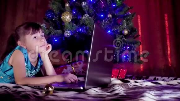 圣诞树下有笔记本电脑的女孩在新年里孩子在一棵树下手提电脑树下的一个小女孩视频的预览图