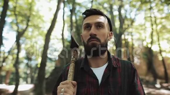 带着斧头走着长胡子的伐木工人戴帽子的人穿过树林寻找树视频的预览图