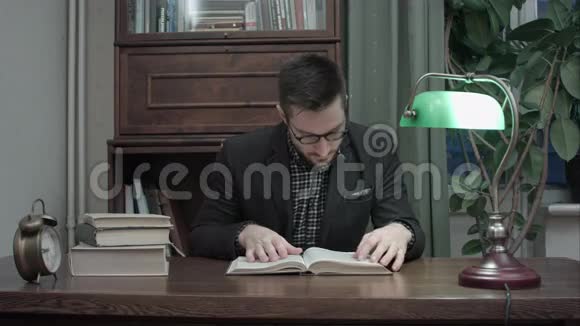 穿西装戴眼镜的年轻人坐在书桌上看书视频的预览图