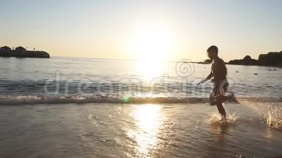 幸福孩子的剪影在日落的海滩上奔跑扬起飞溅慢动作视频的预览图