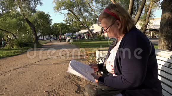在阳光明媚的季节养老金领取者在公园长椅上仔细阅读书籍视频的预览图