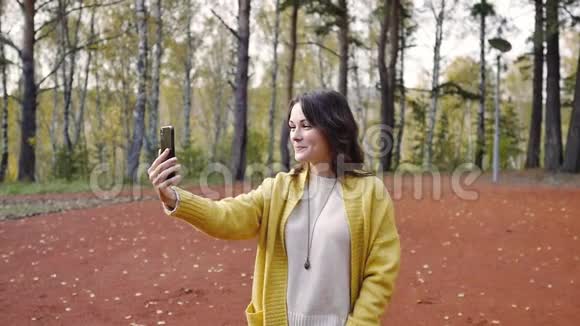 秋天公园里穿着一件带电话的黄色毛衣的年轻女人公园里的女人用手机打电话女孩视频的预览图