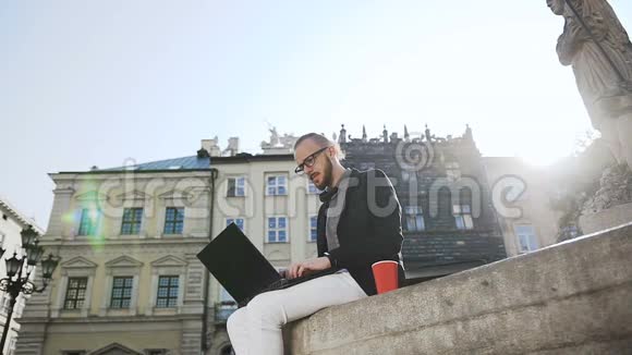 一个戴着眼镜留着胡子的年轻商人在城里的电脑上工作喝咖啡视频的预览图