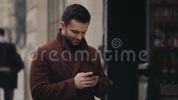 年轻的帅哥穿着时髦的外套站在市中心用他的手机上网视频的预览图