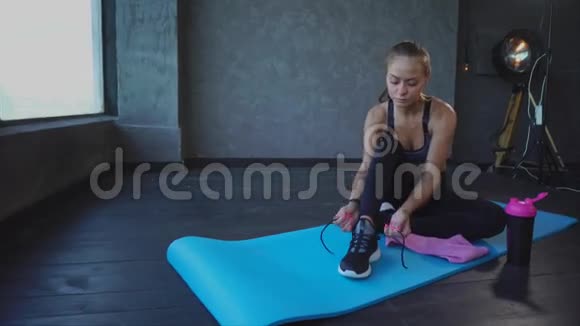 年轻运动员在运动鞋上系鞋带一位女士坐在地毯上做瑜伽视频的预览图