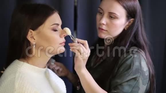 在美容店为年轻女孩化妆过程在模特脸上涂眼影年轻形象视频的预览图