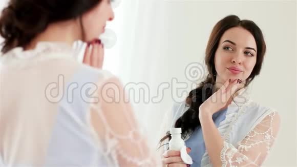漂亮的年轻女人在镜子前用棉签和保湿乳液做面部护理视频的预览图