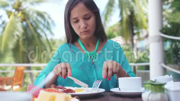 年轻的黑发美女坐在海滩咖啡馆吃早餐慢动作3840x2160视频的预览图