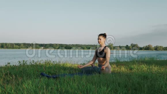 日出时处于莲花位置的漂亮女人早上在湖边做瑜伽的女孩视频的预览图